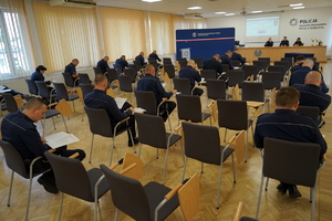 policjanci siedzą na krzesłach, słuchają organizatorów zawodów i przystępują do pisania testu