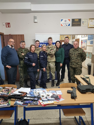 Trzech umundurowanych policjantów stoi. Obok nich stoją cztery osoby ubrane w mundur taktyczny, obok nich stoi mężczyzna .