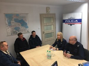 Dwóch umundurowanych policjantów i  trzech mężczyzn, wszyscy siedzą przy stole.