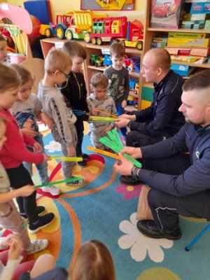 Umundurowani policjanci siedza. Dzieci stoją obok nich.