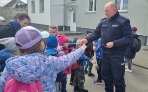 Umundurowany policjant rozdaje odblaski,stoja dzieci.