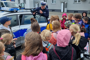 Policjant umundurowany stoi. Obok stoją dzieci.