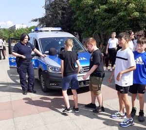 Umundurowany policjant stoi przy radiowozie, obok stoją dzieci.