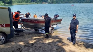 Umundurowany policjant stoi nad brzegiem jeziora, obok stoją osoby obok łódki.