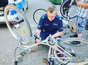 Policjant umundurowany kuca, przed nim leży rower.