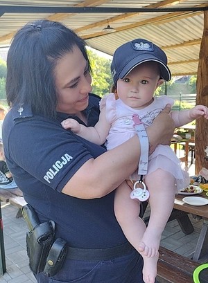 Umundurowany policjant stoi. Trzyma na rękach małe dziecko.