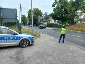 Umundurowany policjant stoi tyłem, obok stoi radiowóz.