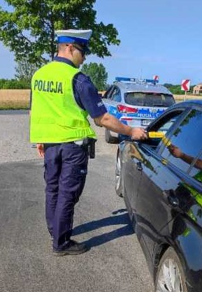 Umundurowany policjant stoi,w ręku trzyma przyrząd do badania stanu trzezwości.