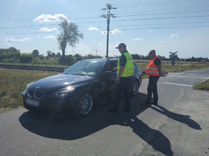 Umundurowany policjant stoi, obok stoi mężczyzna. stoi obok nich samochód.