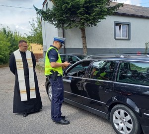 Umundurowany policjant stoi obok samochodu, obok stoi ksiądz.