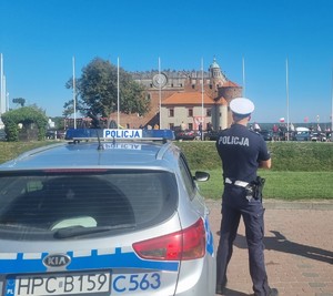 Umundurowany policjant stoi obok radiowozu.