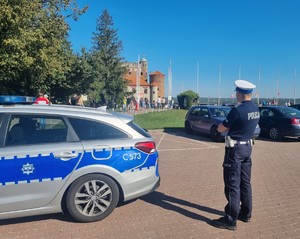 Umundurowany policjant stoi obok radiowozu.