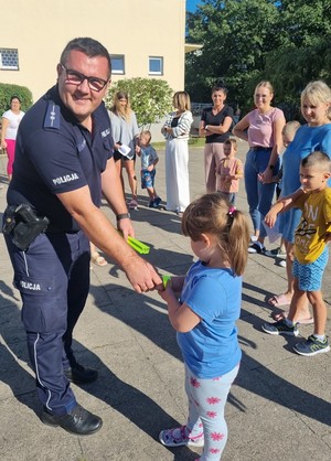 Policjant stoi podaje dziecku odblask.