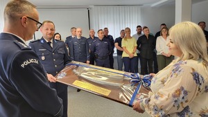 Policjant i pracownik cywilny wręcza upominek emerytowi
